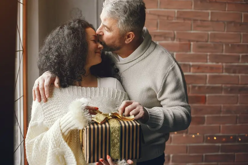 Loving couple exchanging a wrapped holiday gift, capturing a warm and intimate moment — perfect inspiration for a personalized Mixbook photo book for partners.