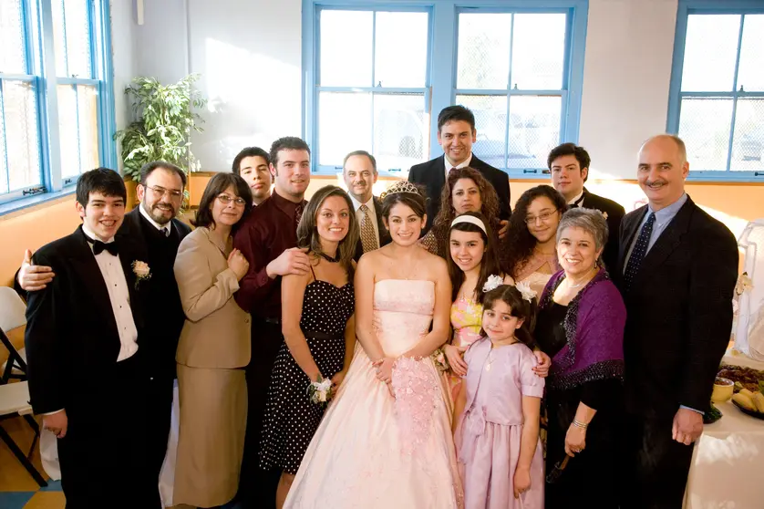 Large family group photo at a quinceañera celebration, with the birthday girl in a pink ball gown and tiara at the center surrounded by smiling relatives