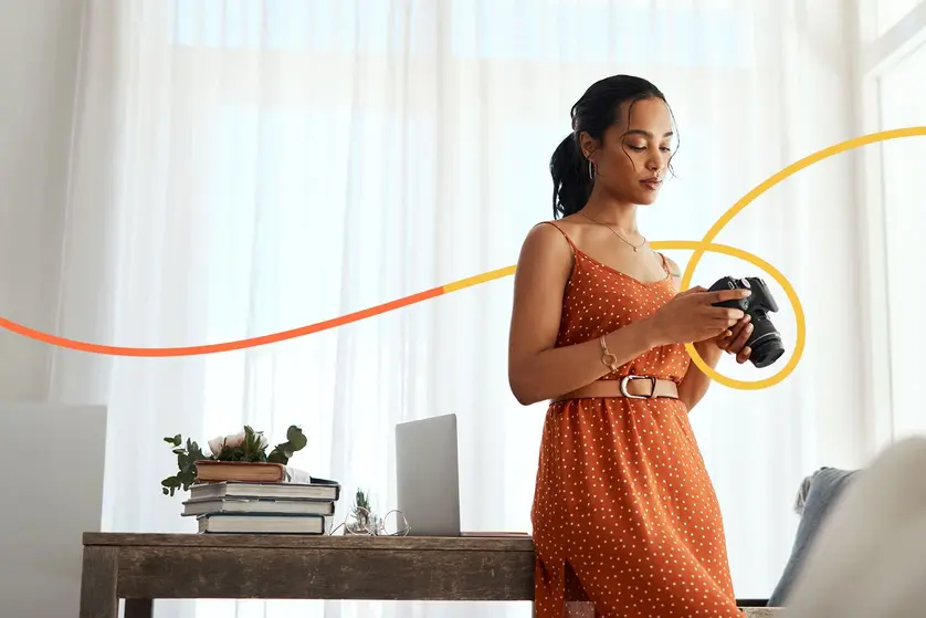 A woman in an orange dress looks at her camera.