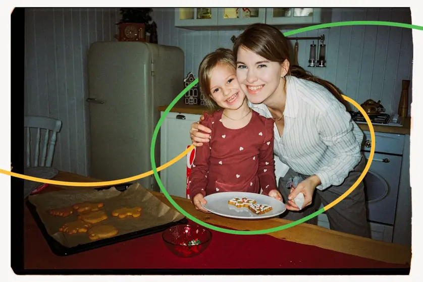 An image of a mother and daughter smiling in the kitchen while decorating holiday cookies together.