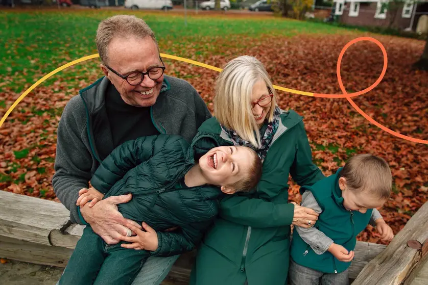 An image of a happy family laughing on a bench surrounded by fall leaves.