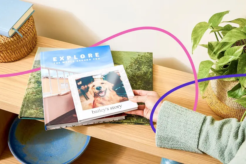 A hand removing a photo book from a stack of photo books on a table.