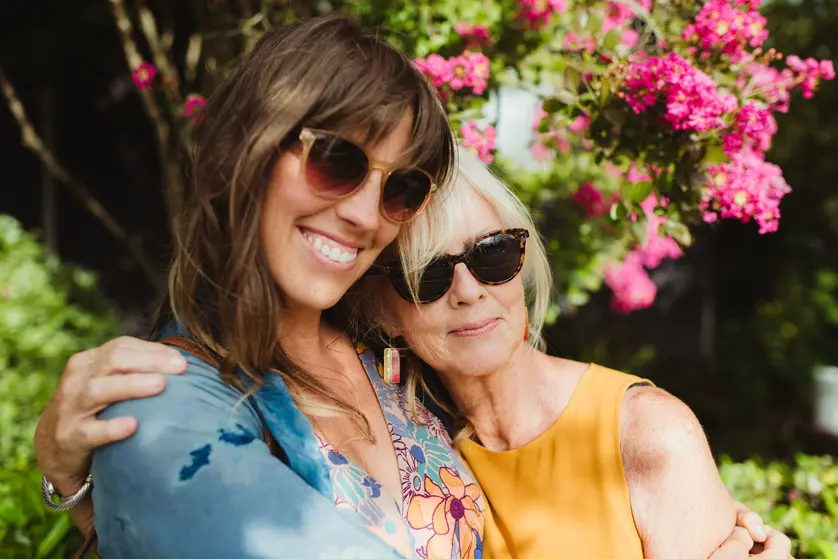 Mother and adult daughter smiling together outdoors surrounded by flowers
