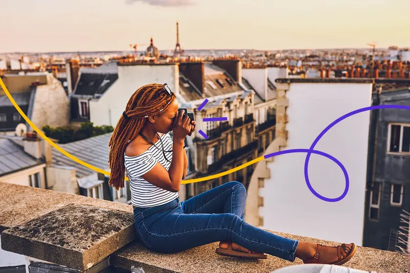 An image of a woman taking a photo while sitting on a rooftop with a city view.