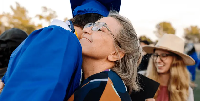 Graduate in cap and gown standing with parent celebrating graduation