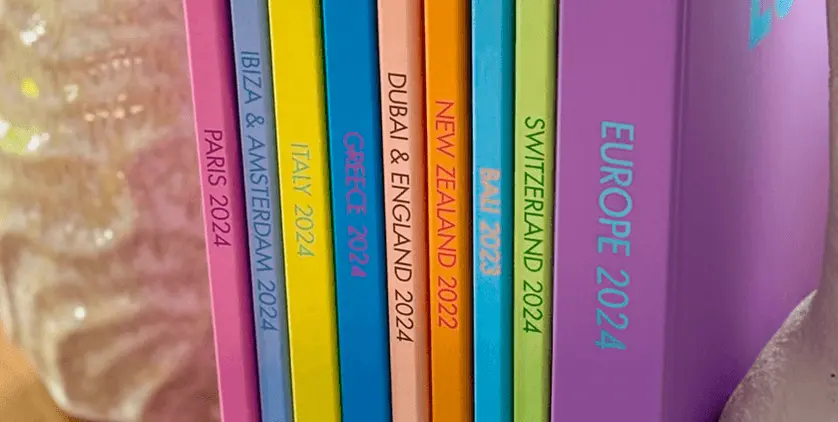 Collection of colorful travel photo books labeled with destinations including Greece, Paris, Italy, Switzerland, and Europe.